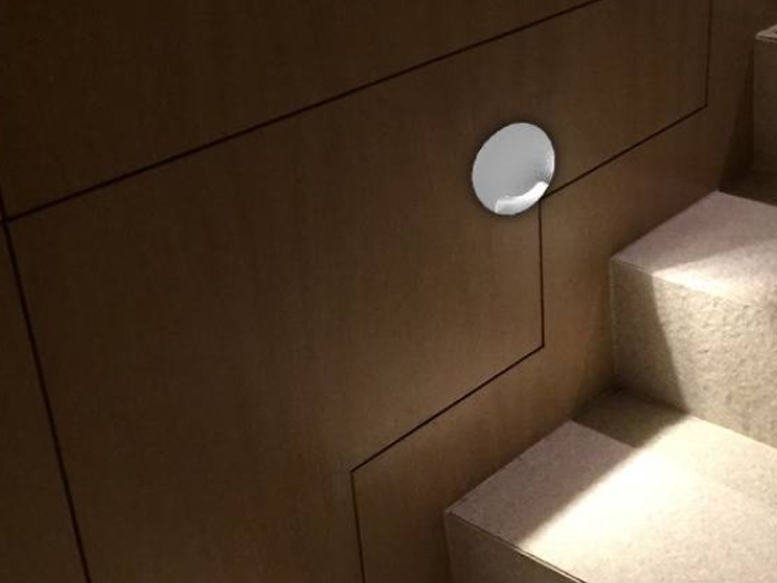 Круглый белый настенный светильник на стене у ступеней