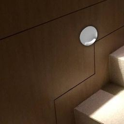 Круглый белый настенный светильник на стене у ступеней